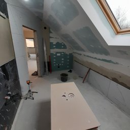 Usługi remontowo wykończeniowe marcin pępek - Poddasze w trakcie wykańczania: płyty gipsowe na skosach, okno dachowe, przygotowana płyta pod umywalkę. Widoczne narzędzia i materiały budowlane.