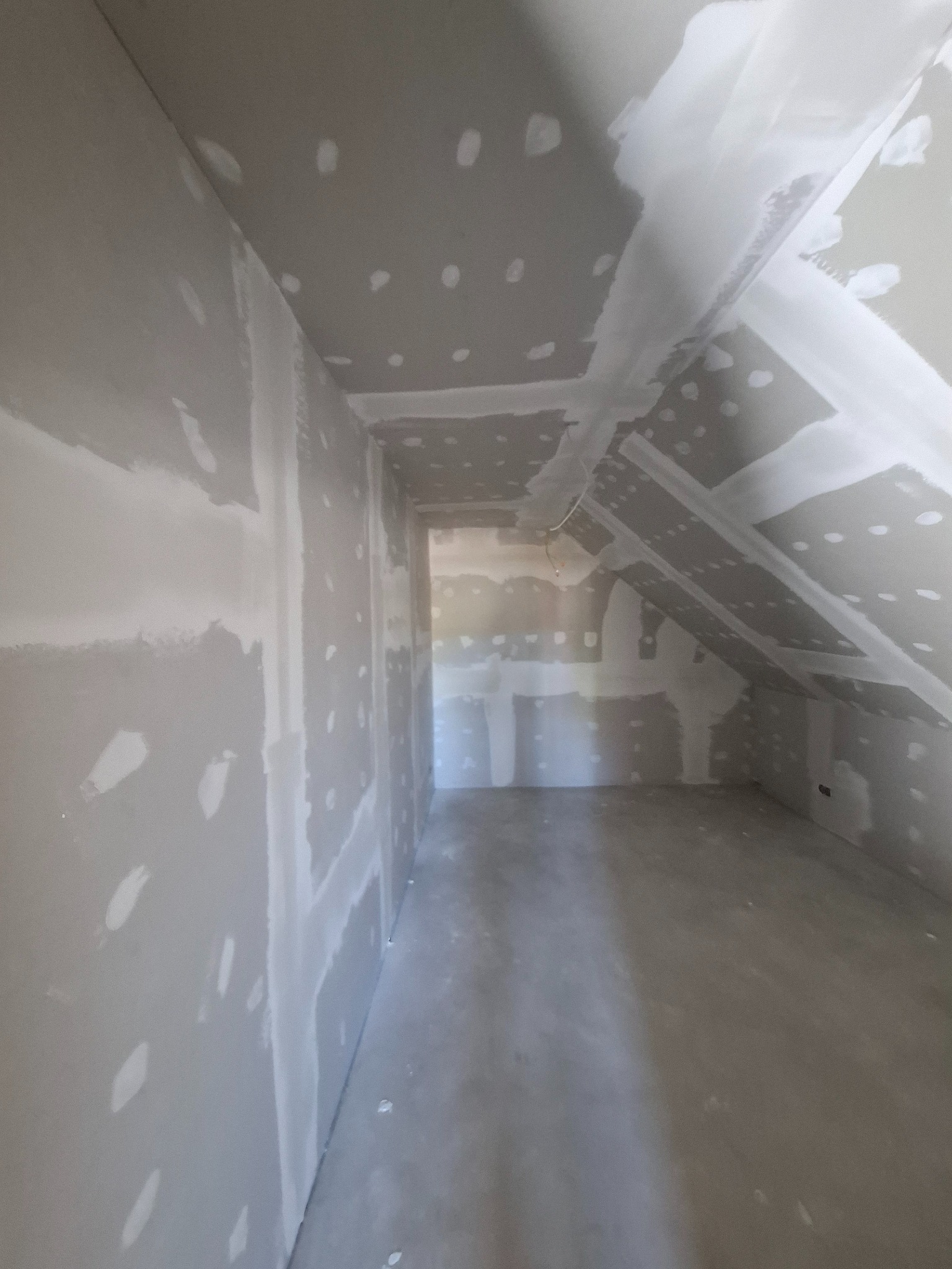 Poddasze po szpachlowaniu, widoczne płyty karton-gips z nałożoną warstwą szpachli. Skosy dachu i sufitu wykończone, przygotowane do dalszych prac wykończeniowych.