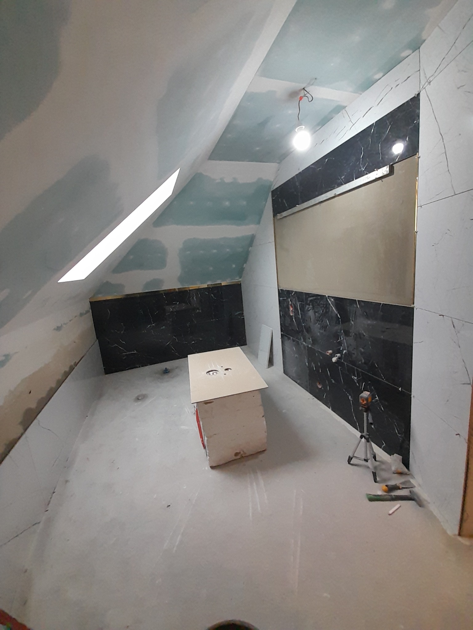 Remont łazienki na poddaszu: ułożone płytki imitujące marmur, sufit i ściany z płyt karton-gips, narzędzia glazurnicze na podłodze. Widok z dołu.