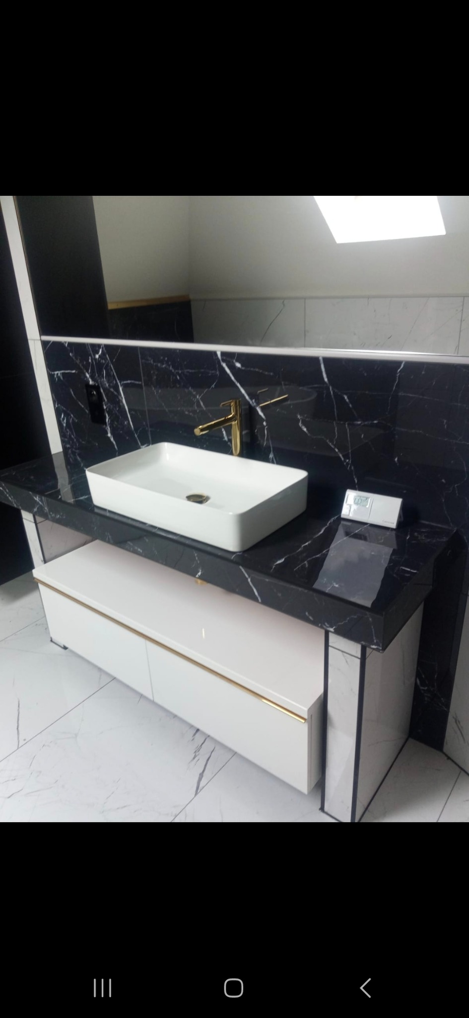 Nowoczesna łazienka z umywalką nablatową, czarnym blatem imitującym marmur i białymi szafkami z złotymi akcentami. Bateria w kolorze złota. Minimalistyczny design.