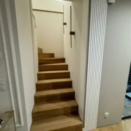 Nowoczesne, drewniane stopnie schodów w jasnym wnętrzu, widok z dołu, parkiet ułożony w jodełkę.