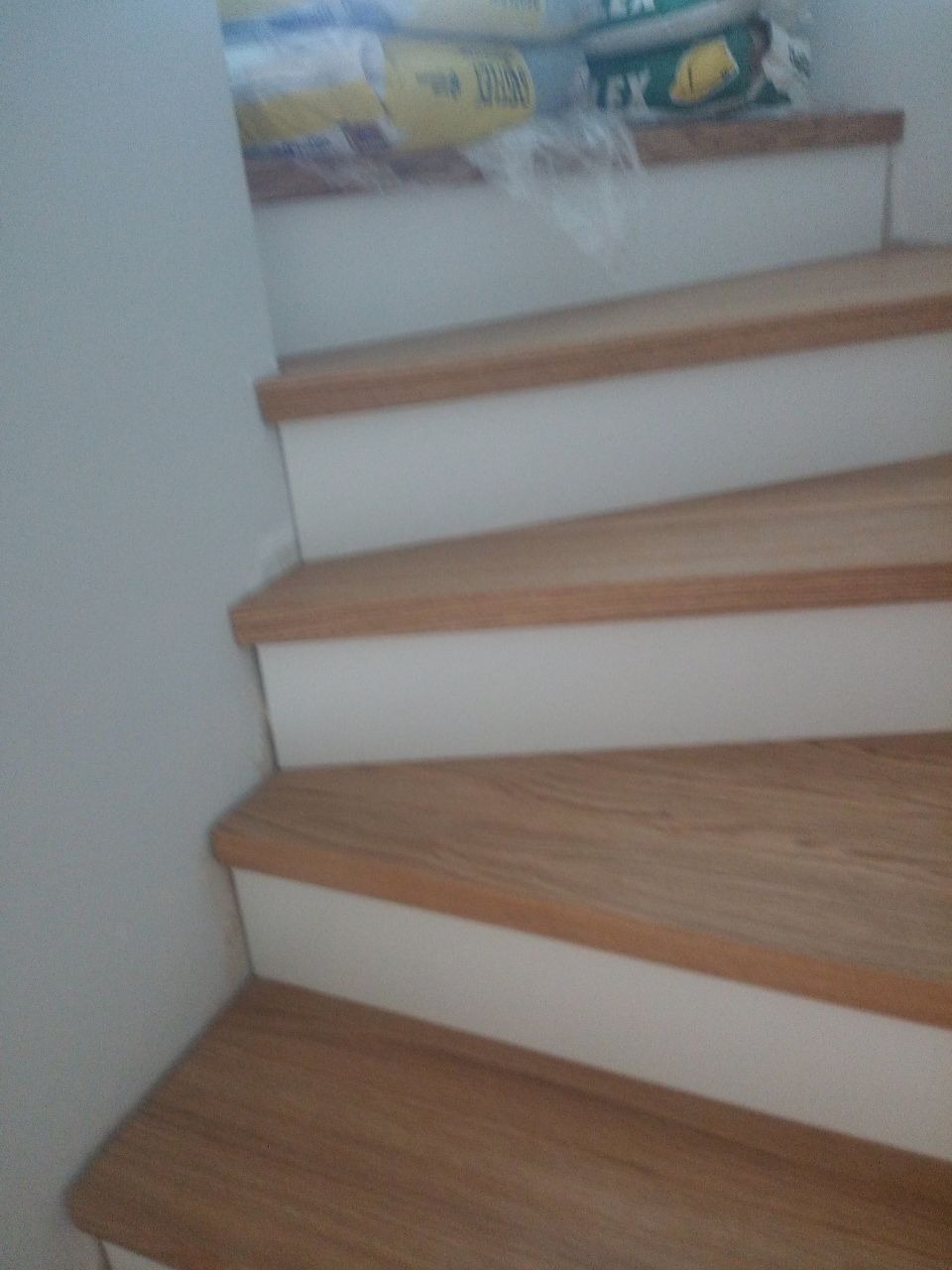 Fragment drewnianych schodów z białymi podstopnicami, widoczne worki z materiałami budowlanymi na górnym stopniu.