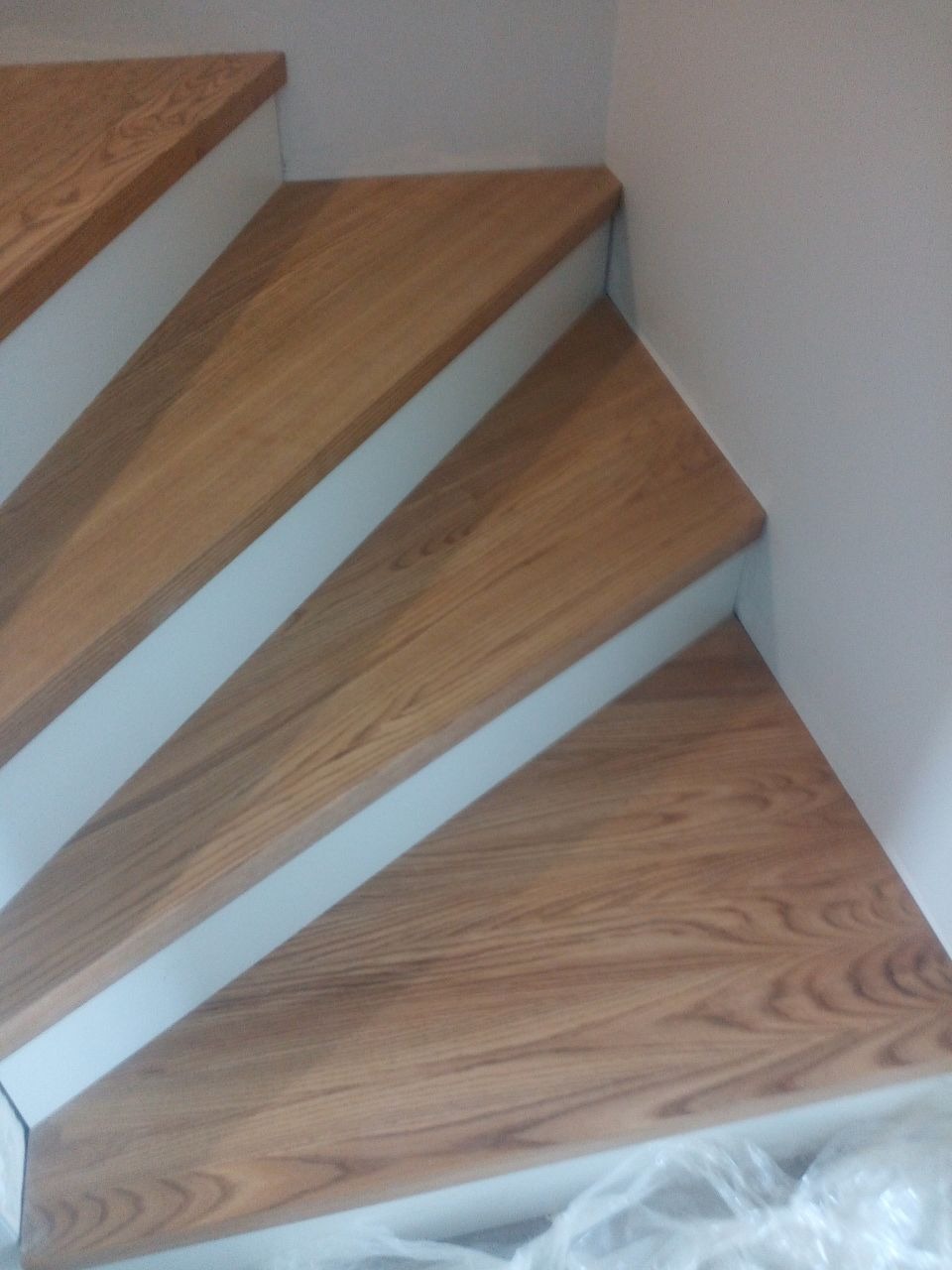 Fragment drewnianych schodów z białymi podstopnicami, widok z góry, częściowo zakryte folią ochronną.