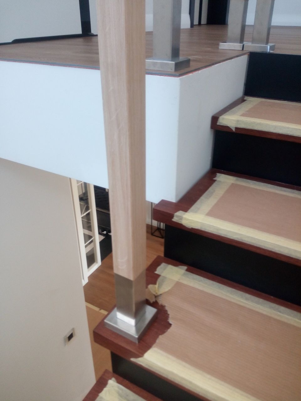 Montaż drewnianych schodów z metalowymi słupkami, zabezpieczonych taśmą malarską na czas prac wykończeniowych.