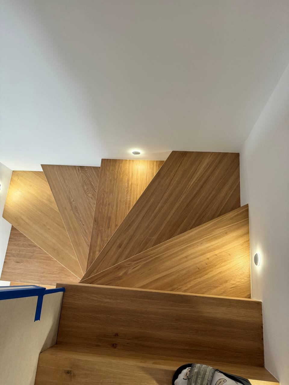 Widok z góry na nowoczesne, dębowe schody z podświetleniem LED w ścianie, wykończone z użyciem taśmy malarskiej, ukazujące unikalny wzór słojów drewna.