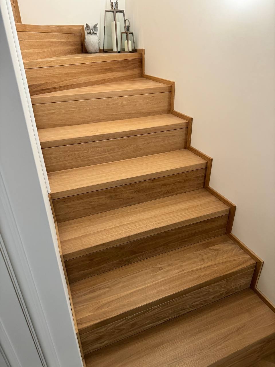 Jasne, drewniane stopnie schodów z widocznym usłojeniem, dekorowane figurką sowy i lampionami na górnym stopniu.