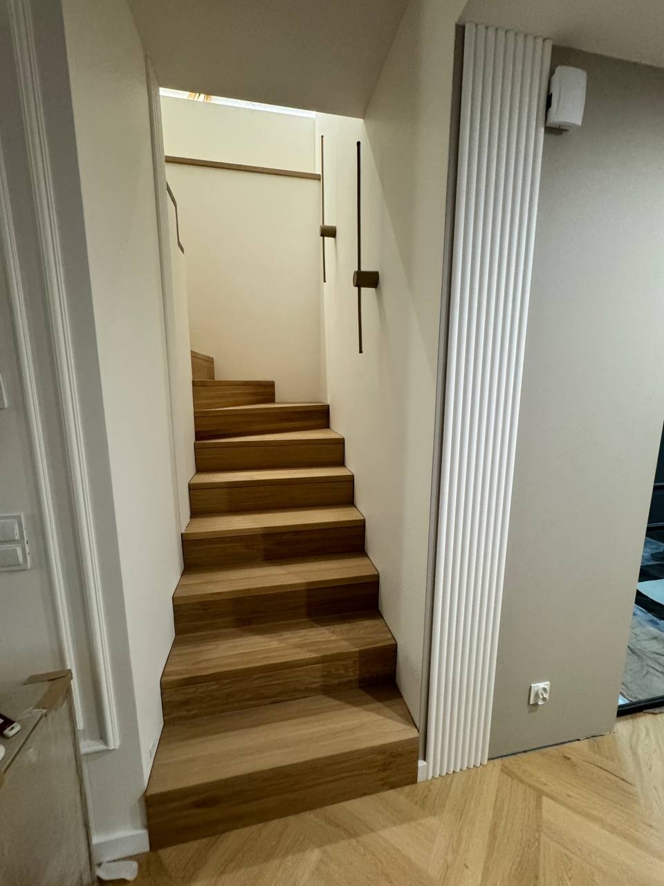 Nowoczesne, drewniane stopnie schodów w jasnym wnętrzu, widok z dołu, parkiet ułożony w jodełkę.