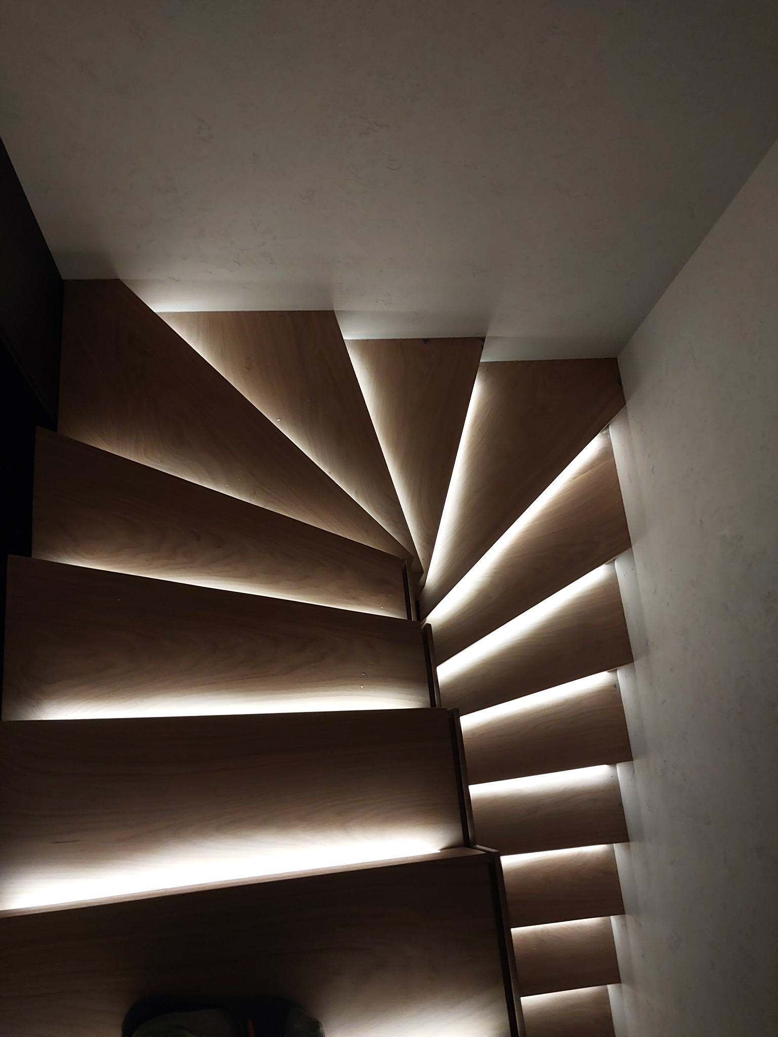 Drewniane schody spiralne z podświetleniem LED od spodu każdego stopnia, tworzące efektowne, ciepłe światło.