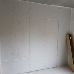 Usługi remontowo budowlane BUDSOB - Wnętrze w trakcie montażu płyt kartonowo-gipsowych, widoczne płyty przykręcone do ściany, szpachlowane łączenia, karton z panelami pod ścianą.
