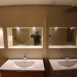 Usługi remontowo budowlane BUDSOB - Wykończona łazienka z dwiema umywalkami nablatowymi, lustrami z oświetleniem LED i beżowymi płytkami ściennymi. W lustrze odbija się osoba robiąca zdjęcie.