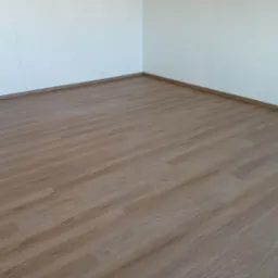 Jasne panele podłogowe imitujące drewno, ułożone w rogu pomieszczenia z białymi ścianami i listwami przypodłogowymi.