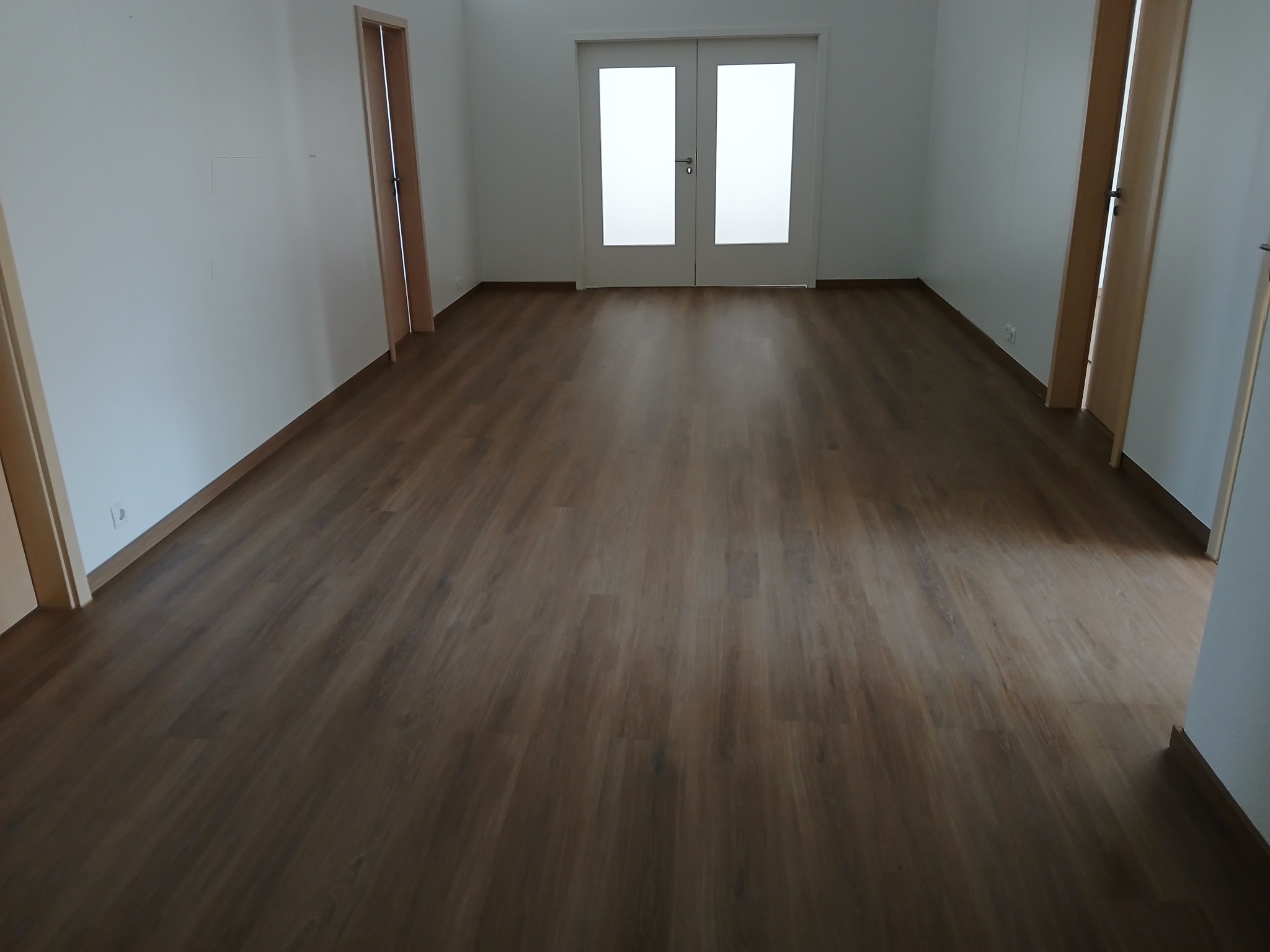 Nowo ułożone panele podłogowe w pustym, jasnym pomieszczeniu z białymi ścianami i trzema parami drzwi.