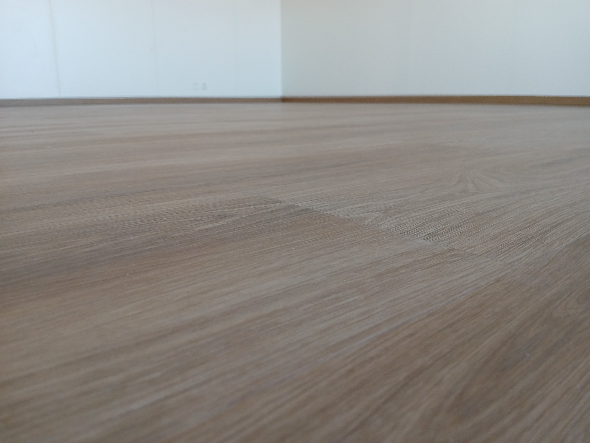 Ułożone panele podłogowe w odcieniach jasnego drewna, widoczne listwy przypodłogowe, białe ściany w tle.