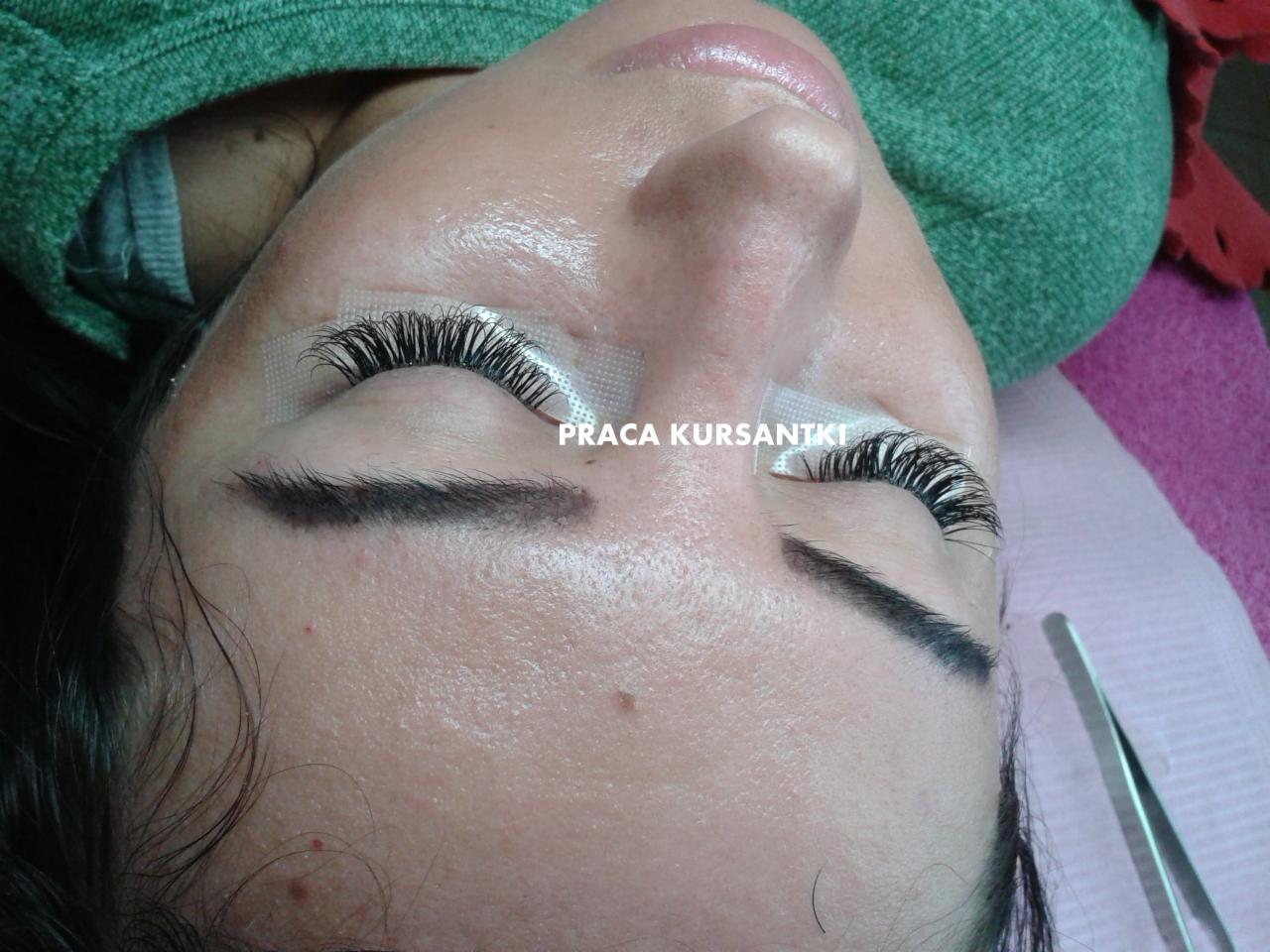 Zbliżenie na oko z przedłużonymi rzęsami, zabezpieczone taśmą, widoczne pęsety, ujęcie z góry, praca kursantki.