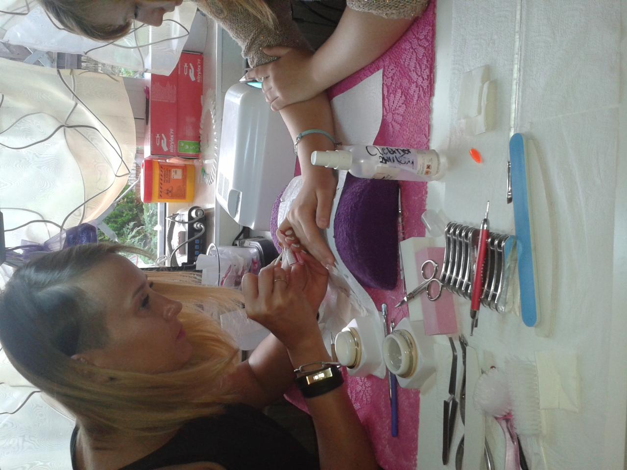 Kobieta wykonuje zabieg na stopie klientki, widoczne narzędzia do pedicure, preparaty kosmetyczne i dłonie stylistki w trakcie pracy.