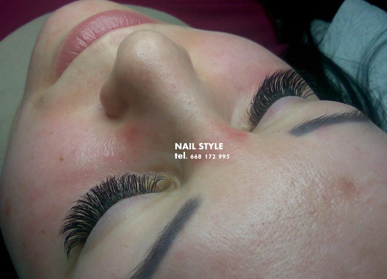 Zbliżenie na twarz kobiety leżącej z zamkniętymi oczami, prezentujące przedłużone, gęste rzęsy w stylu 'kocie oko' oraz delikatny makijaż brwi. W tle widoczny fragment podkładu lub kosmetyku...