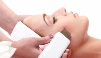 Zabieg oczyszczania skóry twarzy za pomocą urządzenia do peelingu kawitacyjnego, białe tło, widoczna dłoń osoby wykonującej zabieg z fioletowym lakierem do paznokci.