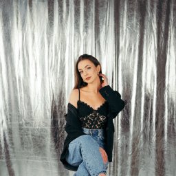 Jakub Chlebda Fotografia - Portret kobiety w czarnej koronkowej bieliźnie i marynarce, siedzącej na tle srebrnej, połyskującej zasłony.