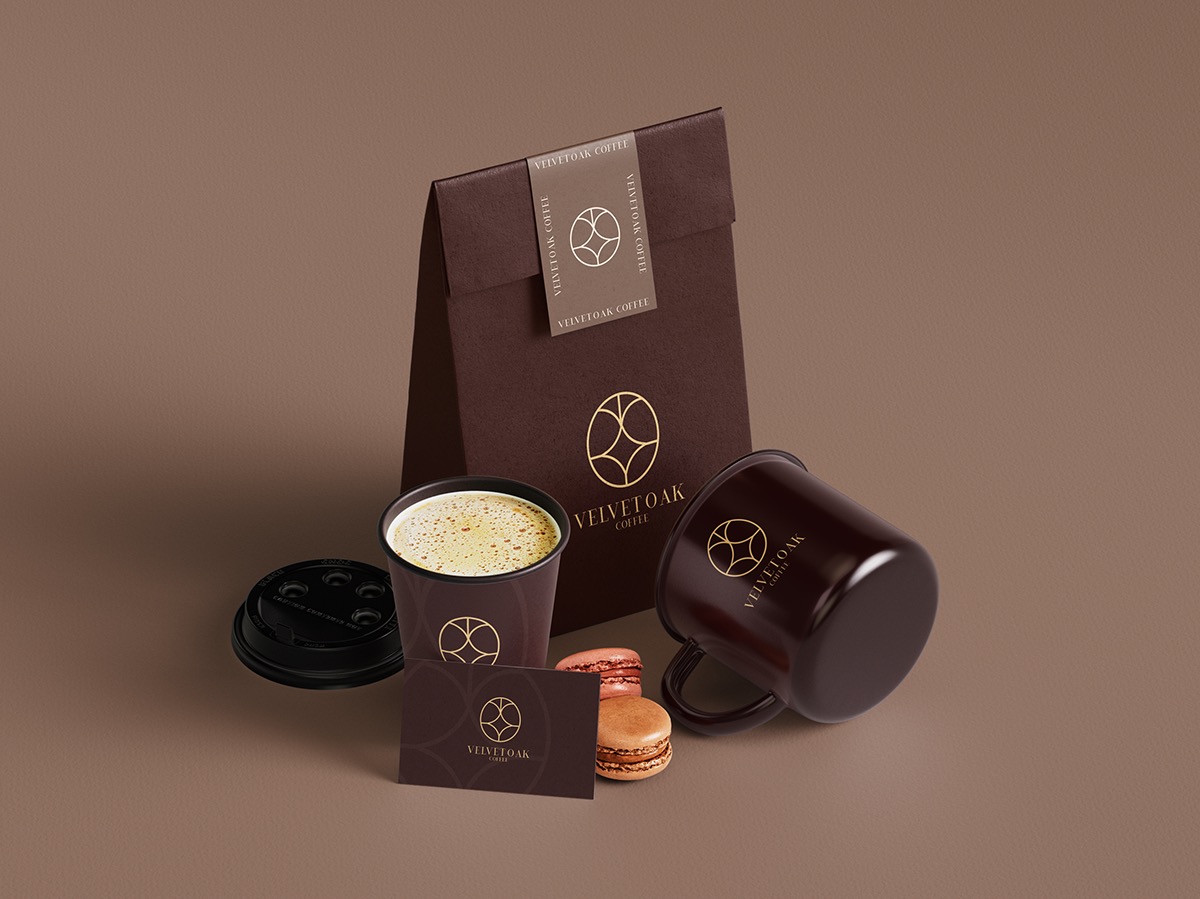 Brązowa torba, kubek emaliowany, papierowy kubek z kawą, wizytówka i dwa makaroniki z logo Velvet Oak Coffee na jednolitym brązowym tle.