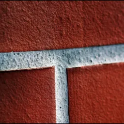 Zbliżenie na fragment ściany z czerwonego klinkieru z jasnoszarą spoiną tworzącą kształt litery T.