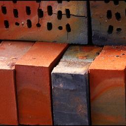 Damiant.com - Cegły klinkierowe ułożone w stos, widoczne różne odcienie czerwieni i szarości, niektóre z otworami, z bliska, z drobnymi pęknięciami i śladami zabrudzeń.