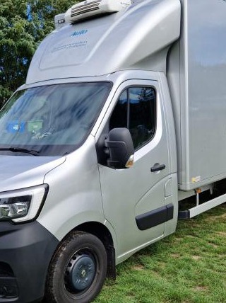 Srebrny bus chłodnia Renault Master z agregatem na dachu, zaparkowany na trawie. Widok z boku, z lekko otwartymi drzwiami.