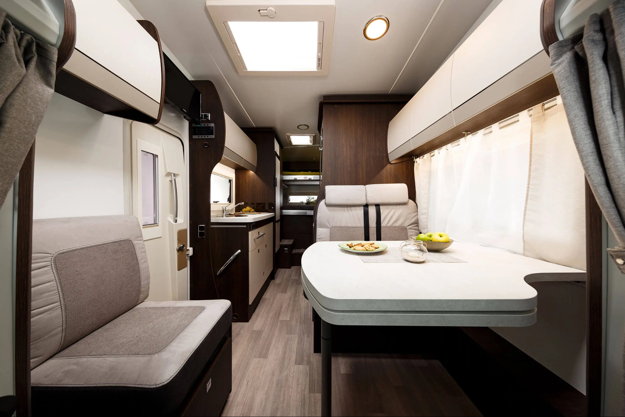 Wnętrze kampera z aneksem kuchennym, stołem z przekąskami i miejscami do siedzenia, utrzymane w stonowanej kolorystyce z elementami drewna.