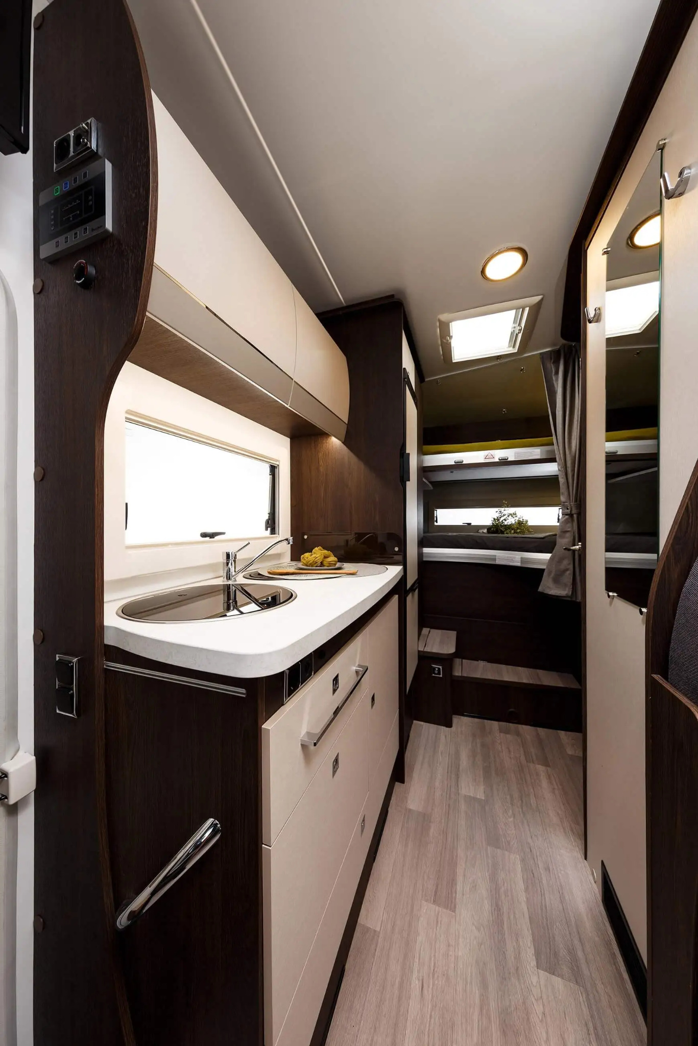 Wnętrze kampera z aneksem kuchennym, łazienką i łóżkiem piętrowym, widok z perspektywy kabiny kierowcy.