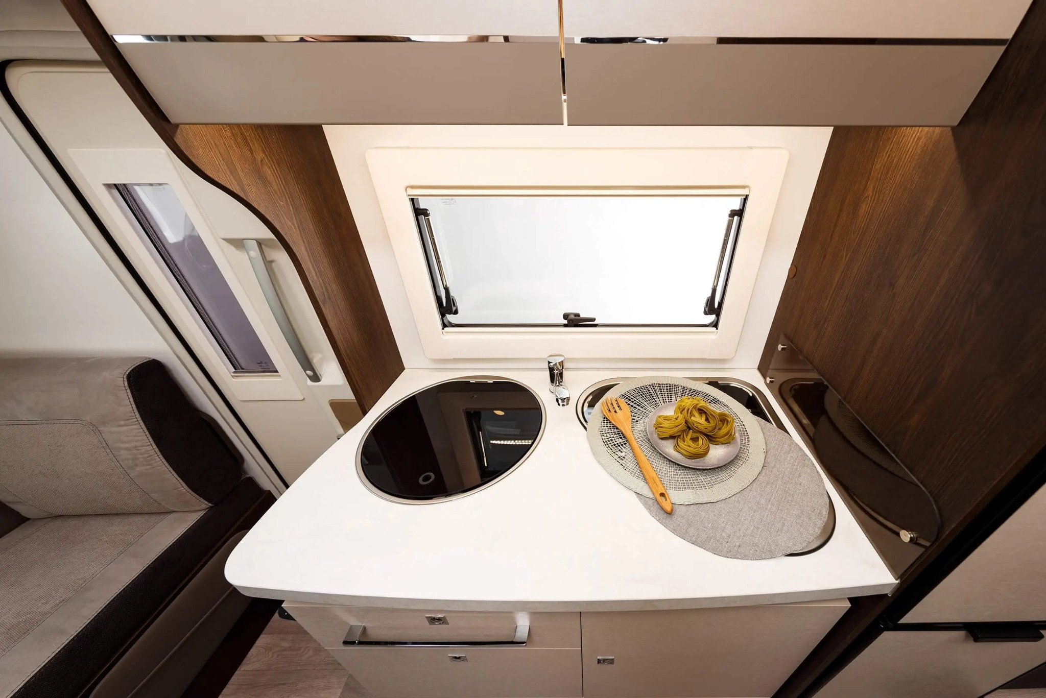 Kompaktowa kuchnia w kamperze z dwupalnikową płytą, zlewem i dekoracyjnym talerzem z makaronem i drewnianym widelcem na blacie.