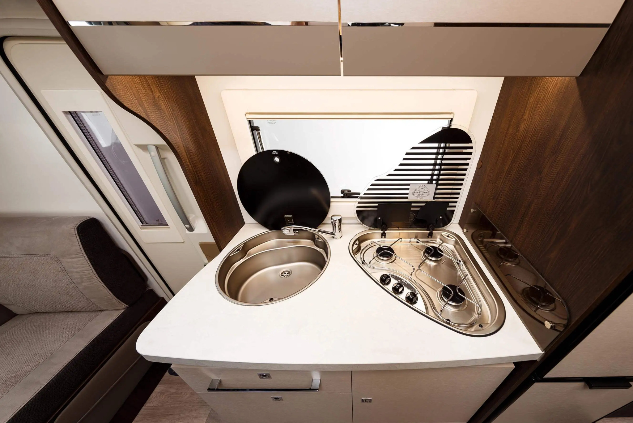 Kompaktowa kuchnia w kamperze z blatem zlewem i dwupalnikową kuchenką gazową, zamkniętą szklaną pokrywą z czarno-białym wzorem.