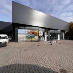 Mycie okien salonu samochodowego Fiat, widoczna drabina oparta o szybę, narzędzia i pachołki na chodniku.