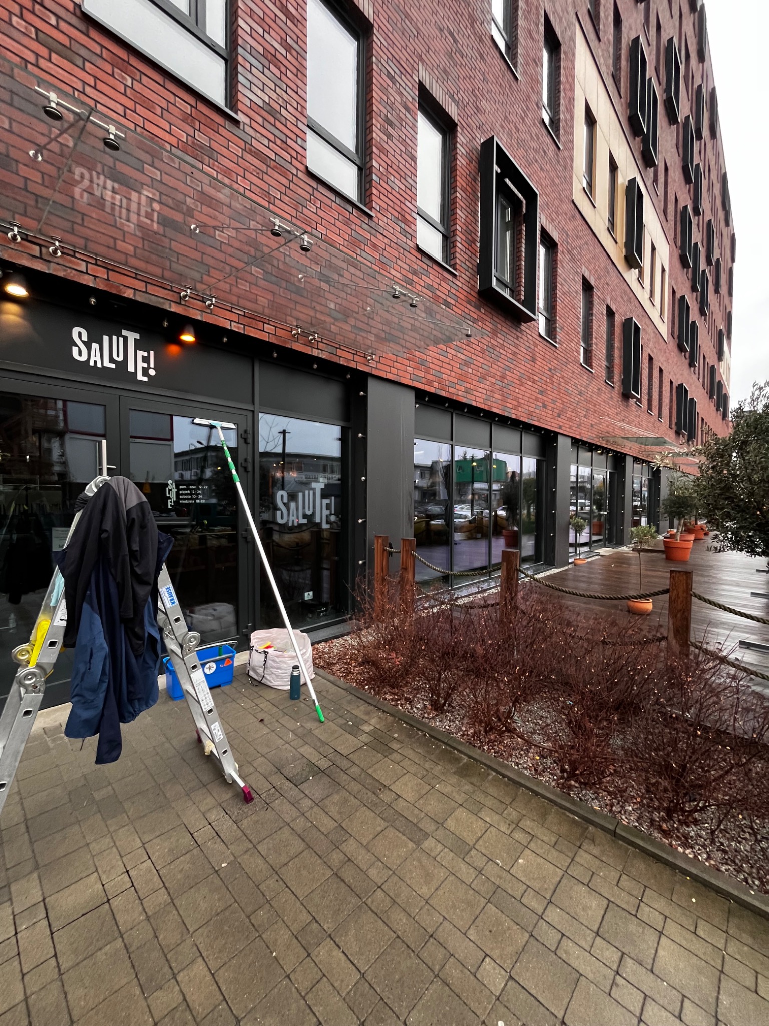 Zewnętrzne okna restauracji Salute! czyszczone za pomocą drabiny, myjki teleskopowej i niebieskiego wiadra z płynem