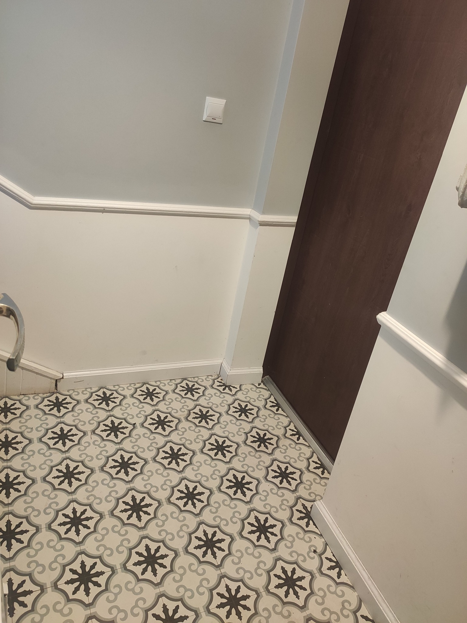 Wzorzysta, kremowo-szara podłoga z motywem kwiatowym w wykończonym pomieszczeniu, widok z góry, brązowe drzwi w tle.