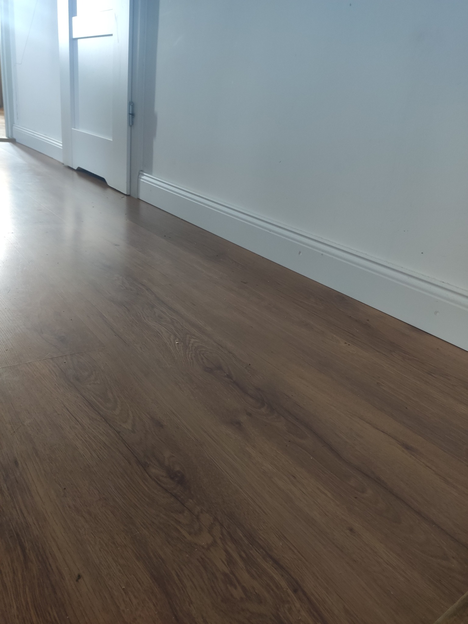 Ułożona podłoga z paneli drewnopodobnych wzdłuż białej ściany z listwą przypodłogową, widoczne drzwi wewnętrzne.