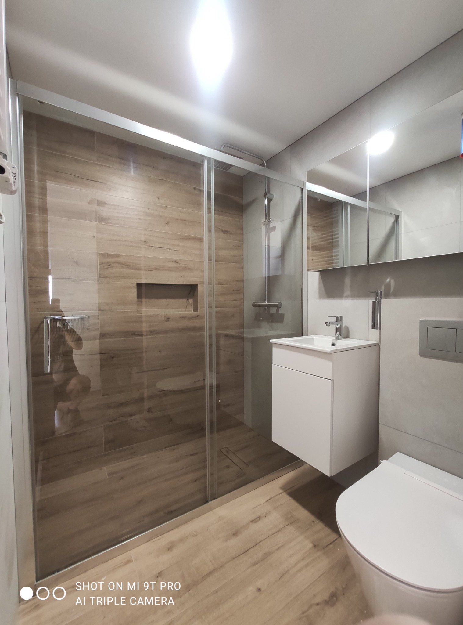 Nowoczesna łazienka po remoncie w Gorzowie Wielkopolskim. Kabina prysznicowa typu walk-in z drewnopodobnymi płytkami, biała umywalka z szafką i lustro.