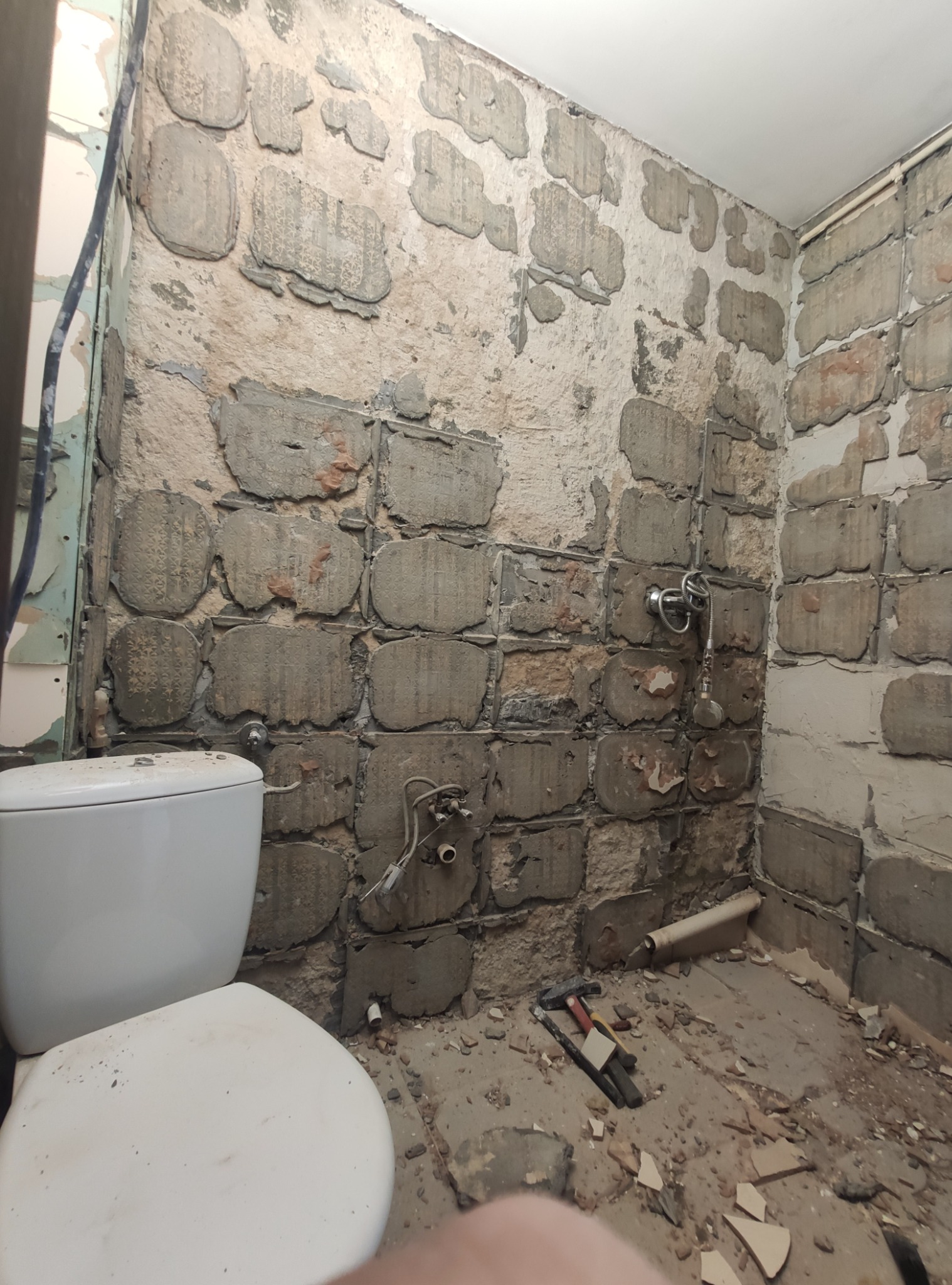 Demontaż płytek w łazience, widoczne fragmenty starej instalacji wodnej, przygotowanie do remontu. Na podłodze gruz i narzędzia.