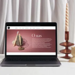 Laptop wyświetlający stronę internetową gabinetu stomatologicznego z zakładką 'O nas', obok świeca w szklanym świeczniku i beżowe wazony na białym obrusie.