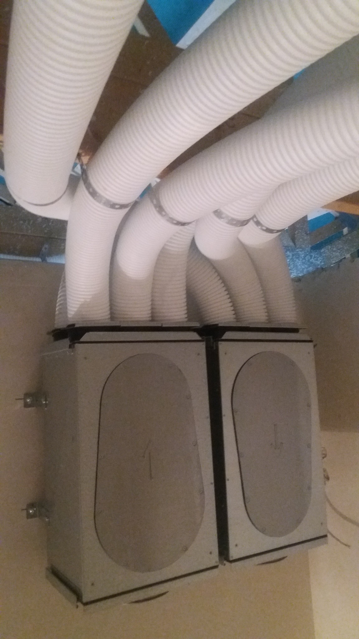 Dwa moduły centrali wentylacyjnej z podłączonymi, elastycznymi przewodami wentylacyjnymi, zamocowane do sufitu.