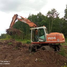 RENEX Ireneusz Kwiatkowski - Pomarańczowa koparka Atlas 1404 z otwartą kabiną podnosi korzenie drzew na wykarczowanym terenie, z zielonym lasem w tle pod pochmurnym niebem.