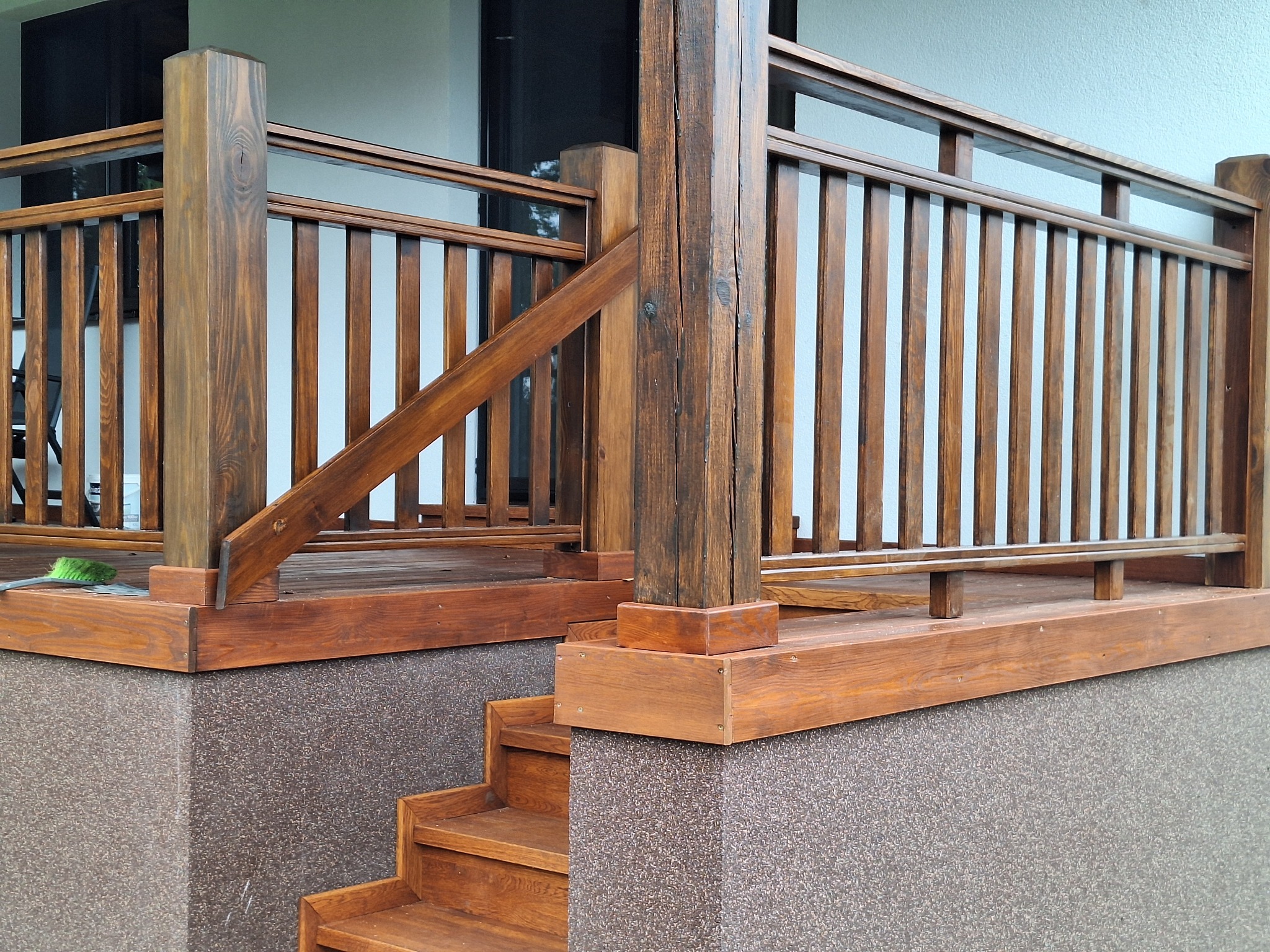 Zewnętrzne, drewniane schody z balustradą na tarasie, widoczne słupki z wyraźnym usłojeniem drewna, brązowy kamień elewacyjny.