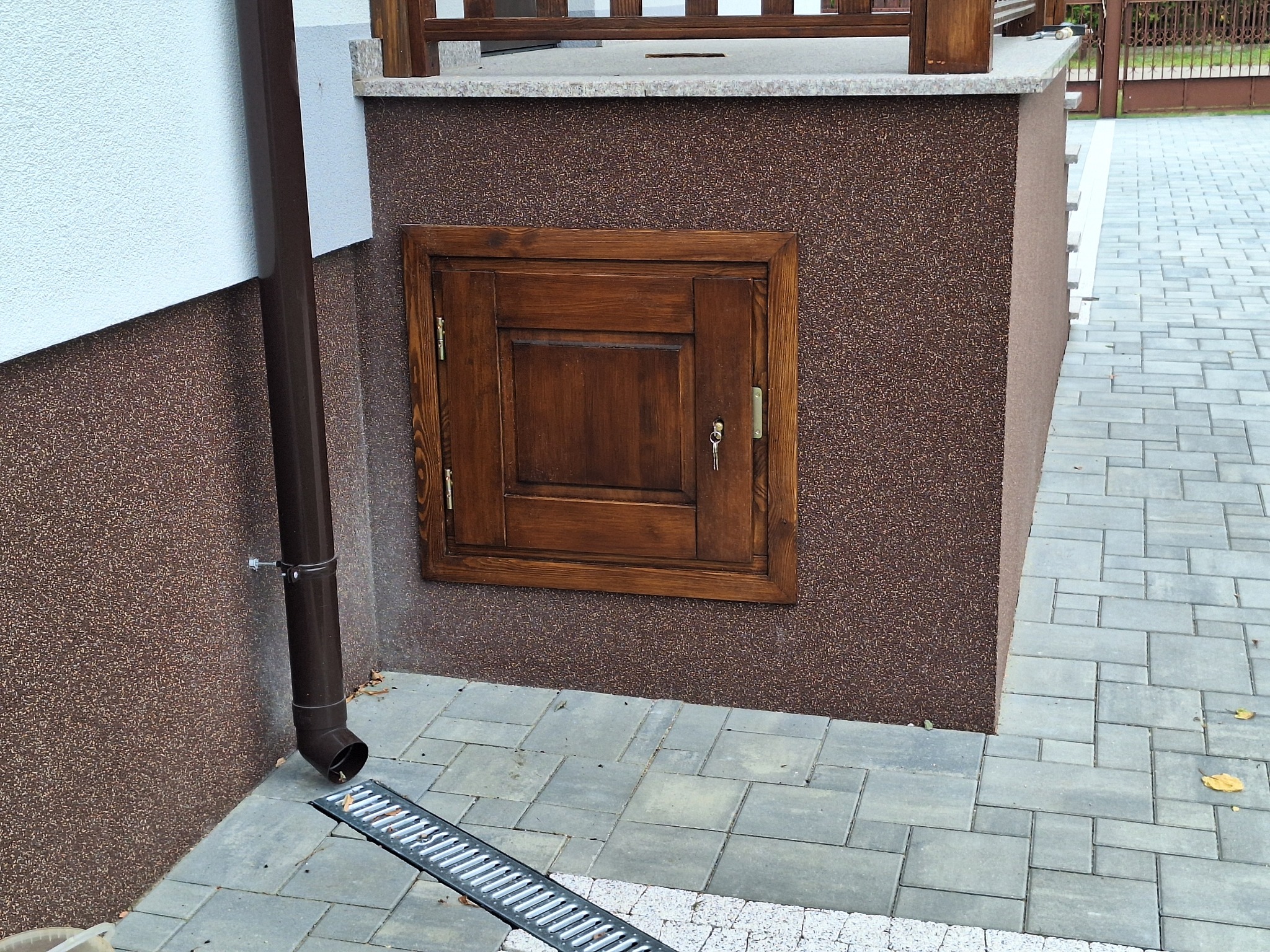 Małe, drewniane drzwi z zamkiem i kluczem w piwnicy, obok rynna spustowa, na zewnątrz budynku.