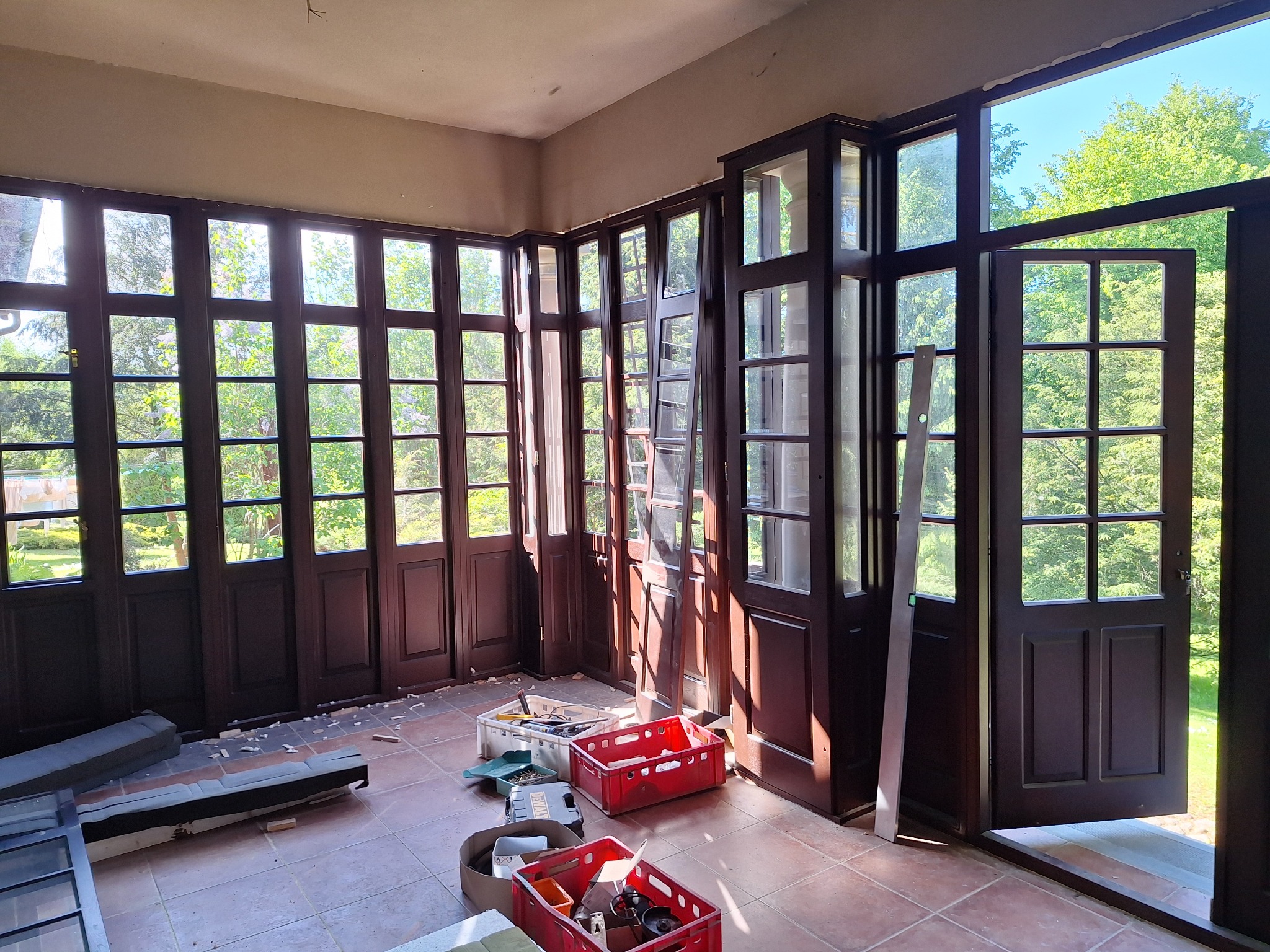 Wnętrze z licznymi, ciemnymi drzwiami z szybami, częściowo otwartymi, w trakcie montażu lub renowacji, widoczne narzędzia i materiały budowlane.