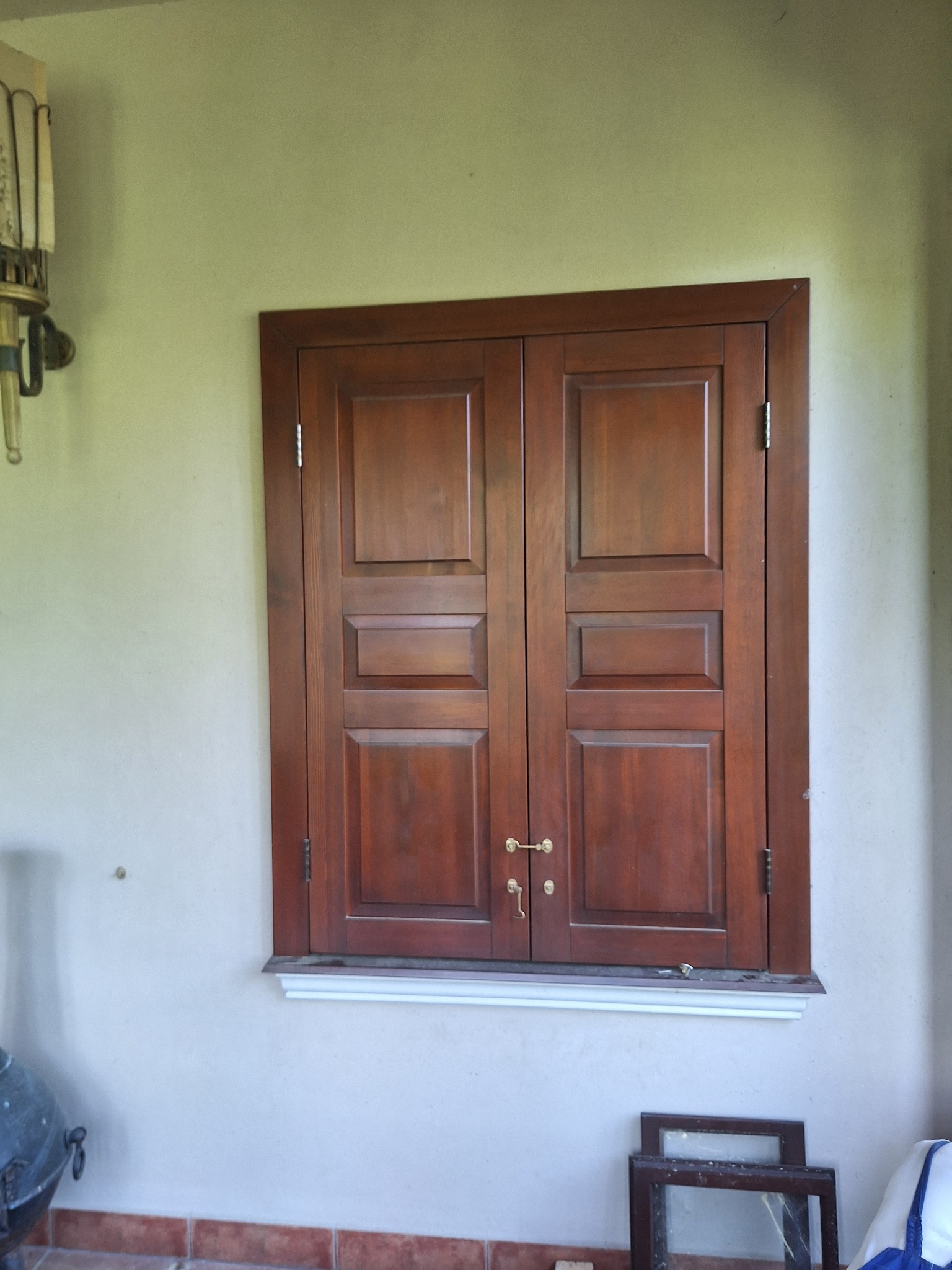 Zabudowane dwuskrzydłowe okno z ciemnego drewna z ozdobnymi płycinami, zamontowane na białym parapecie w jasnym pomieszczeniu, widoczne elementy dekoracyjne na ścianie i ramy okienne na podłodze.