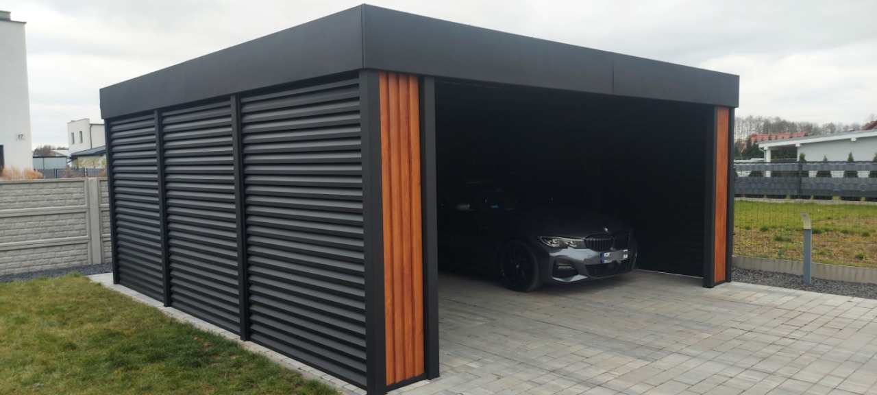 Nowoczesna, czarna wiata garażowa z lamelami i drewnianymi akcentami, na tle kostki brukowej i zieleni. Wewnątrz zaparkowany samochód.