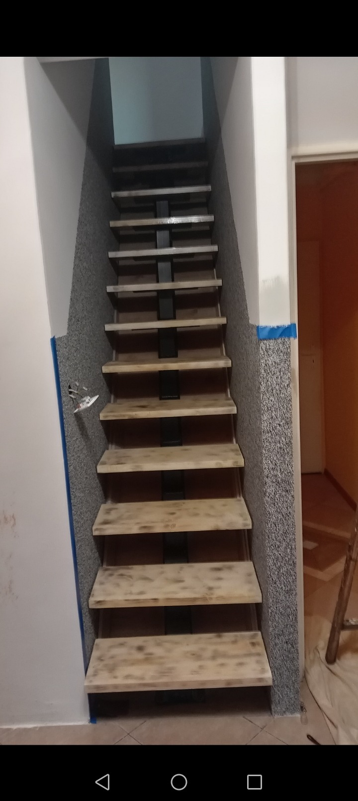 Wnętrze z drewnianymi schodami o metalowej konstrukcji, widok od dołu, ściany wykończone w dwóch odcieniach szarości, widoczna instalacja elektryczna w trakcie prac wykończeniowych, zabezpieczone...