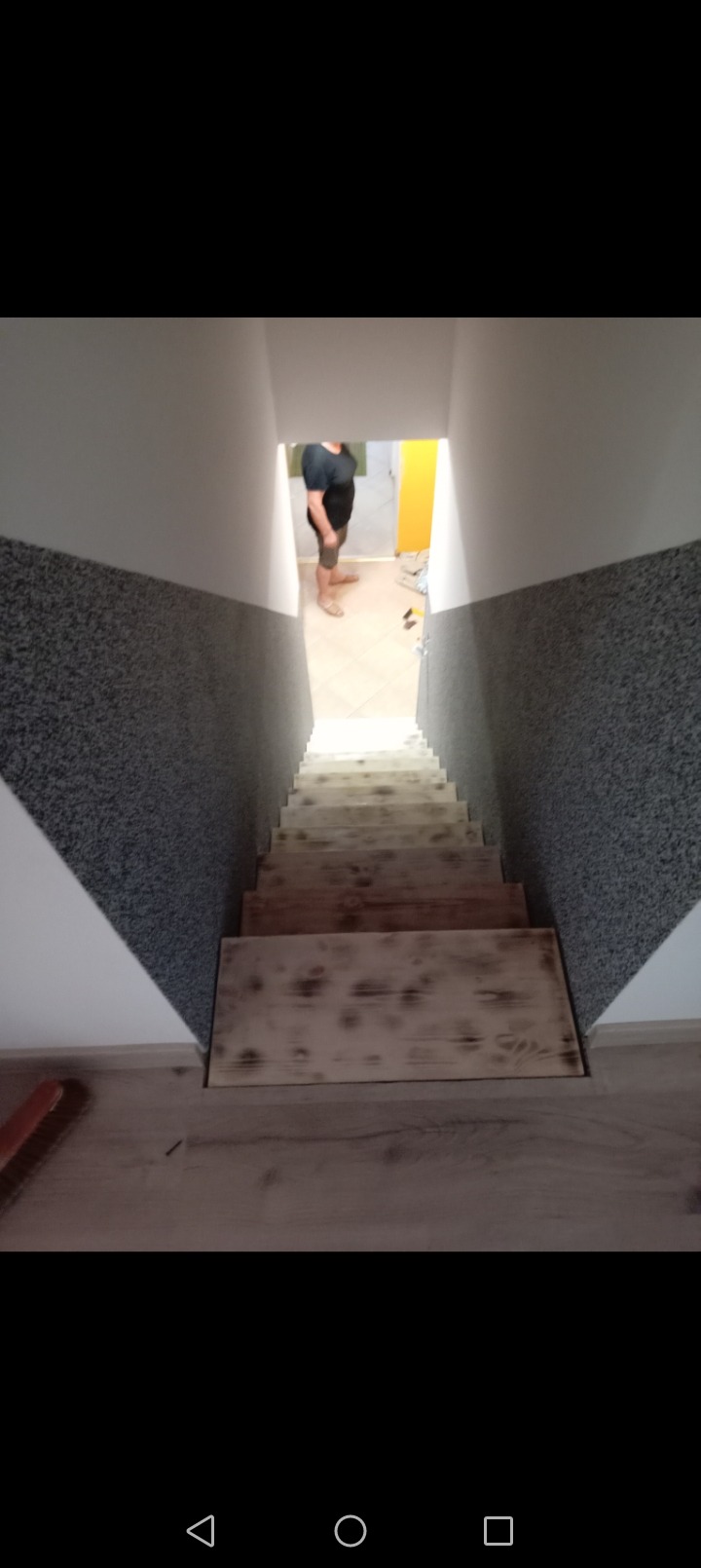 Schody drewniane w trakcie montażu, widok z góry, osoba w tle w jasnym pomieszczeniu.