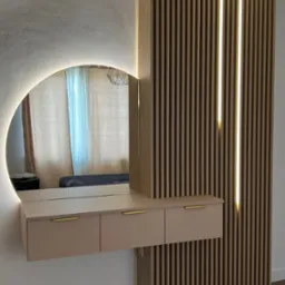 Nowoczesna toaletka z okrągłym lustrem podświetlanym LED, zawieszona na ścianie z drewnianych lameli z wbudowanym oświetleniem liniowym.