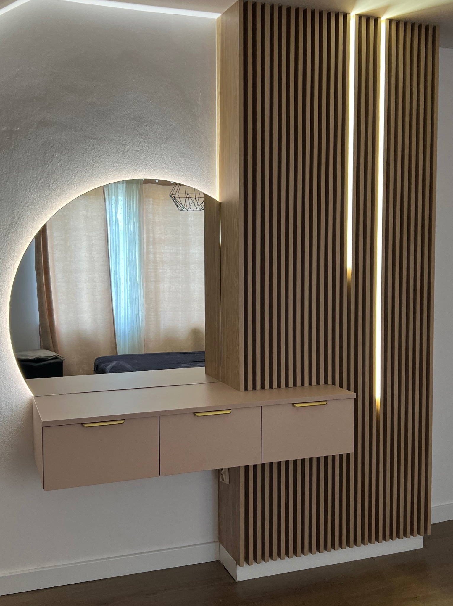 Nowoczesna toaletka z okrągłym lustrem podświetlanym LED, zawieszona na ścianie z drewnianych lameli z wbudowanym oświetleniem liniowym.