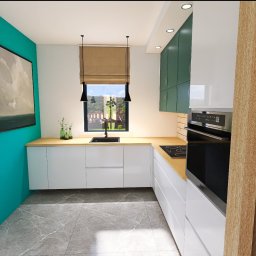 Art Tabor Design Marta Tabor - Wnętrze nowoczesnej kuchni z białymi szafkami, drewnianym blatem i zielonymi górnymi szafkami, oświetlone wiszącymi lampami nad zlewem, z widokiem na zewnątrz przez okno z beżową roletą rzymską.