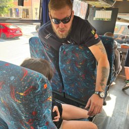 Akademia Reaguj i Ratuj - Instruktor w czarnej koszulce z logo firmy sprawdza stan ucznia siedzącego w autobusie, prawdopodobnie podczas wyjazdu integracyjnego.